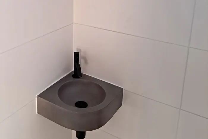 Hoekfonteintje met zwarte kraan in een betegeld toilet